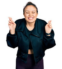 Wall Mural - Young hispanic girl wearing sportswear gesturing finger crossed smiling with hope and eyes closed. luck and superstitious concept.