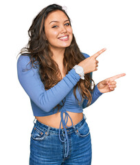 Wall Mural - Young hispanic girl wearing casual clothes smiling and looking at the camera pointing with two hands and fingers to the side.