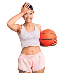 Wall Mural - Young woman holding basketball ball stressed and frustrated with hand on head, surprised and angry face