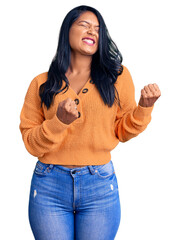 Poster - Hispanic woman with long hair wearing casual winter sweater excited for success with arms raised and eyes closed celebrating victory smiling. winner concept.