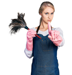 Wall Mural - Beautiful young blonde woman wearing apron holding cleaning duster pointing with finger up and angry expression, showing no gesture