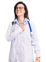 Wall Mural - Young beautiful woman wearing doctor stethoscope and glasses cheerful with a smile of face pointing with hand and finger up to the side with happy and natural expression on face