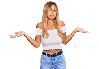 Canvas Print - Beautiful blonde young woman wearing casual white tshirt clueless and confused expression with arms and hands raised. doubt concept.