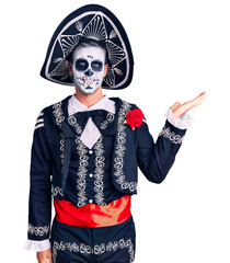 Sticker - Young man wearing day of the dead costume over background smiling cheerful presenting and pointing with palm of hand looking at the camera.