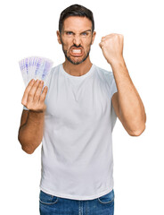 Sticker - Handsome man with beard holding 20 swedish krona banknotes annoyed and frustrated shouting with anger, yelling crazy with anger and hand raised