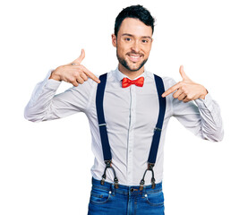 Poster - Hispanic man with beard wearing hipster look with bow tie and suspenders looking confident with smile on face, pointing oneself with fingers proud and happy.