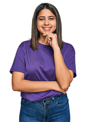 Sticker - Young hispanic girl wearing casual purple t shirt looking confident at the camera with smile with crossed arms and hand raised on chin. thinking positive.