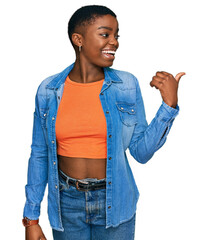 Sticker - Young african american woman wearing casual clothes smiling with happy face looking and pointing to the side with thumb up.