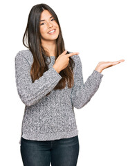 Wall Mural - Young brunette woman wearing casual winter sweater amazed and smiling to the camera while presenting with hand and pointing with finger.