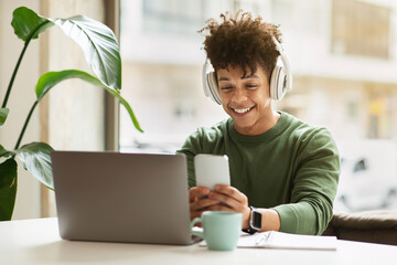 Wall Mural - Cheerful young black guy student using gadgets at cafe