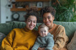 © Helena GARCIA - pareja de mujeres lesbianas posando junto a su hijo pequeño, sentadas en el sofá de su salón, sobre fondo de estancia desenfocado