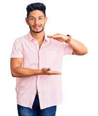 Sticker - Handsome latin american young man wearing casual summer shirt gesturing with hands showing big and large size sign, measure symbol. smiling looking at the camera. measuring concept.