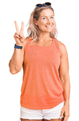 Wall Mural - Middle age fit blonde woman wearing casual summer clothes and sunglasses showing and pointing up with fingers number two while smiling confident and happy.