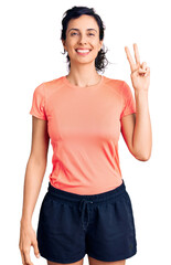 Canvas Print - Young beautiful hispanic woman wearing sportswear smiling with happy face winking at the camera doing victory sign. number two.