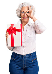 Wall Mural - Senior grey-haired woman holding gift smiling happy doing ok sign with hand on eye looking through fingers