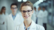 Beautiful young woman scientist wearing white coat and glasses in modern Medical Science Laboratory with Team of Specialists on background 