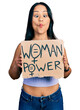 Beautiful hispanic woman holding woman power banner making fish face with mouth and squinting eyes, crazy and comical.