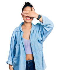 Wall Mural - Beautiful hispanic woman wearing casual denim jacket and glasses smiling and laughing with hand on face covering eyes for surprise. blind concept.