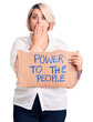 © Krakenimages.com - Young blonde plus size woman holding power to the people banner covering mouth with hand, shocked and afraid for mistake. surprised expression