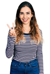 Wall Mural - Beautiful hispanic woman wearing casual striped shirt showing and pointing up with fingers number two while smiling confident and happy.