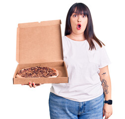 Canvas Print - Young plus size woman holding delivery pizza box scared and amazed with open mouth for surprise, disbelief face