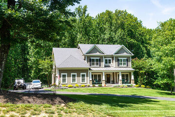 Residential two-story detached house on the edge of the forest with a green lawn in front