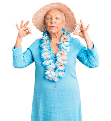 Wall Mural - Senior beautiful woman with blue eyes and grey hair wearing summer hat and hawaiian lei relax and smiling with eyes closed doing meditation gesture with fingers. yoga concept.