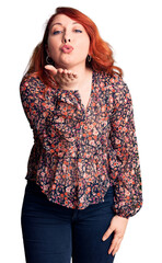 Poster - Young beautiful redhead woman wearing casual t-shirt looking at the camera blowing a kiss with hand on air being lovely and sexy. love expression.