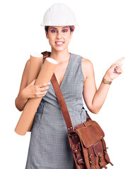 Poster - Young beautiful woman wearing architect hardhat and leather bag holding blueprints smiling happy pointing with hand and finger to the side