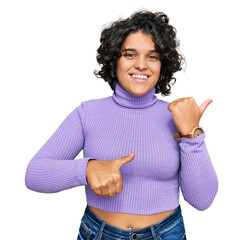 Canvas Print - Young hispanic woman with curly hair wearing casual clothes pointing to the back behind with hand and thumbs up, smiling confident