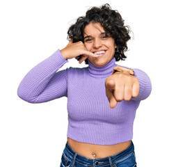 Canvas Print - Young hispanic woman with curly hair wearing casual clothes smiling doing talking on the telephone gesture and pointing to you. call me.