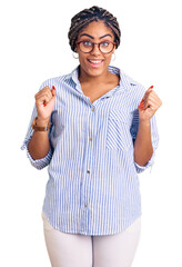 Wall Mural - Young african american woman with braids wearing casual clothes and glasses celebrating surprised and amazed for success with arms raised and open eyes. winner concept.
