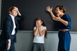 Schoolgirl and her mother yell at the teacher standing at the blackboard. 