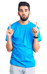 Wall Mural - Young handsome man with beard wearing casual t-shirt pointing up looking sad and upset, indicating direction with fingers, unhappy and depressed.