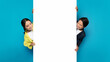 Asian man and woman playfully peeking around a large white vertical banner