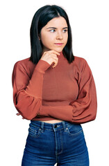 Poster - Young brunette woman with blue eyes wearing elegant sweater with hand on chin thinking about question, pensive expression. smiling with thoughtful face. doubt concept.