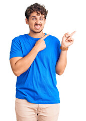 Wall Mural - Young handsome man with curly hair wearing casual clothes pointing aside worried and nervous with both hands, concerned and surprised expression