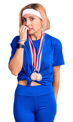 Poster - Young blonde woman wearing winner medals looking stressed and nervous with hands on mouth biting nails. anxiety problem.