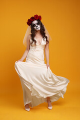 Poster - Young woman in scary bride costume with sugar skull makeup and flower crown posing on orange background. Halloween celebration