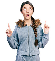 Canvas Print - Young brunette girl with long hair wearing casual sweatshirt amazed and surprised looking up and pointing with fingers and raised arms.