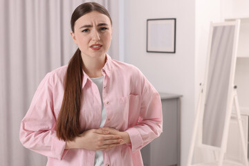 Wall Mural - Young woman suffering from stomach pain at home. Space for text