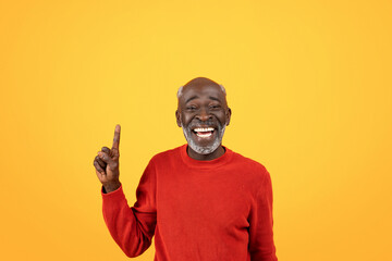 Wall Mural - Joyful elderly Black man with white beard laughing and pointing upwards, wearing red sweater