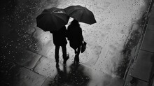  Two People Holding Umbrellas Walking Down A Street In The Rain On A Rainy Day In A Black And White Photo.