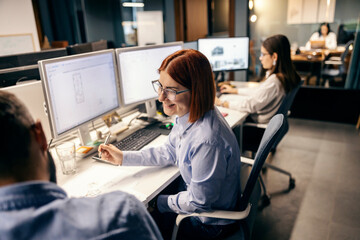 Wall Mural - A happy architect is sitting at office and working on blueprints while smiling at colleague.