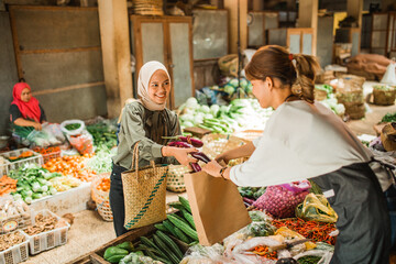 Wall Mural - female asian customer getting help from greengrocery seller to putting vegetables in paperbag