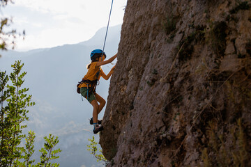 A determined and strong boy climber climbs a steep mountain wall. Extreme sports and rock climbing.