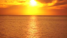 A Red Burning Sunset Over Sea With Rocky Volcanic Cliff. Abstract Nature Summer Ocean Sea Background. Small Waves On Golden Warm Water Surface With Bokeh Lights From Sun. Weather And Climate Change