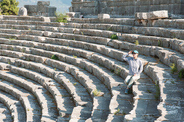 Wall Mural - Tourist woman sitting on the steps of The ancient Greek amphitheater at the ancient City