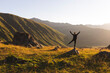 © Westend61 - Carefree woman with arms raised standing on rock in front of mountains at sunset
