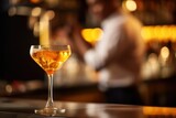 Fototapeta  -  a close up of a wine glass on a bar with a person in the background in a blurry photo.